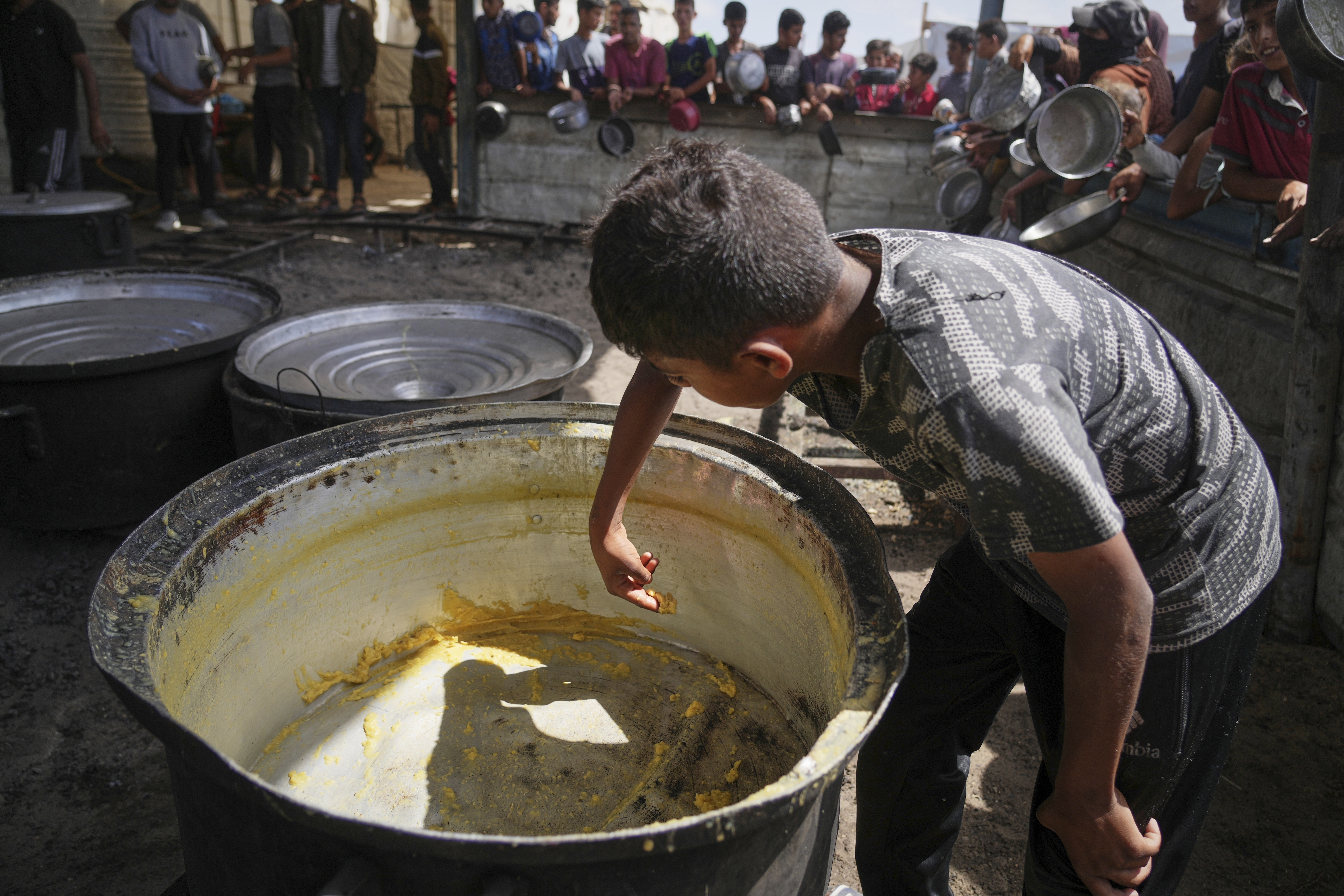 A boy scrapes leftovers from an empty pot after all the meals were distributed at a community kitchen in Khan Younis, southern Gaza Strip, Wednesday, May 14, 2025.<br />(Abdel Kareem Hana / AP Photo)