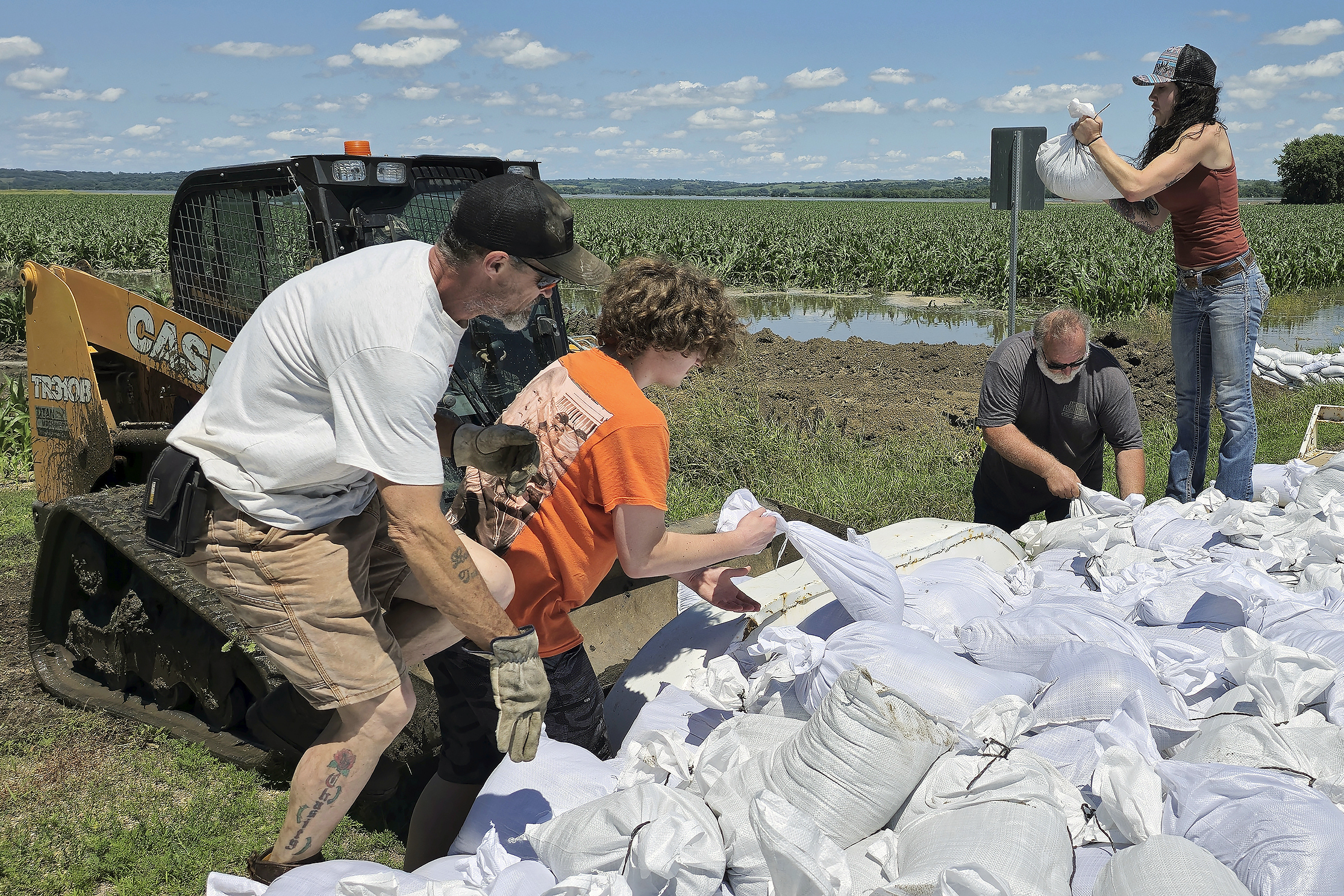 Volunteers toss sandbags into the bucket of a loader that will take them to be used to reinforce a berm on the northeast side of Jefferson, South Dakota, Sunday, June 23, 2024. The sandbag effort is an attempt to keep floodwaters from the Big Sioux River from inundating the town.<br /> (Tim Hynds / Sioux City Journal via AP)