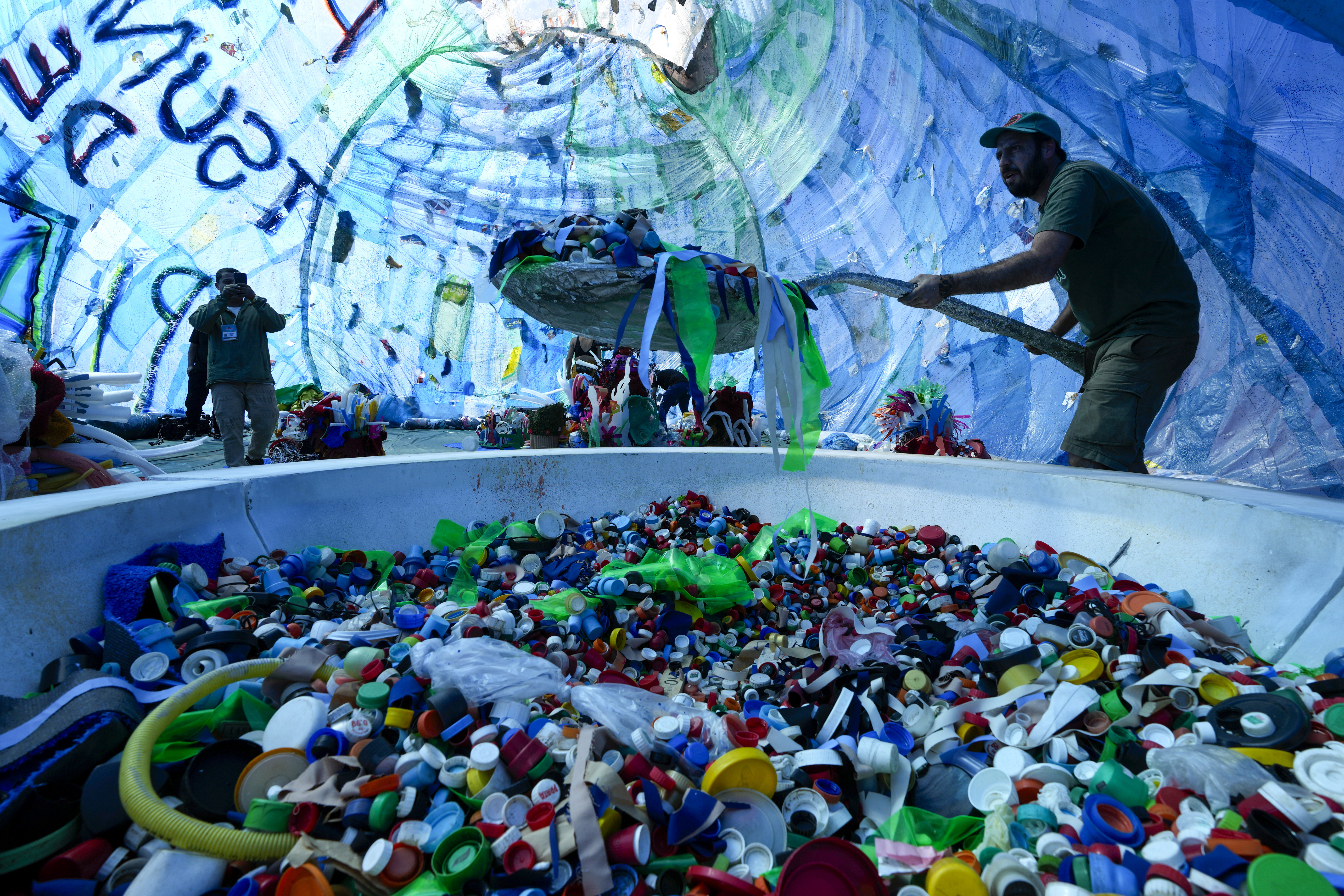 Environmental activist Mundano performs the cleaning of plastic from a beach as part of his immersive installation titled &quot;Plastic Tsunami&quot; on the sidelines of the Zero Waste meeting hosted by the National Museum of the Republic in Brasilia, Brazil, Tuesday, June 25, 2024.<br />(Eraldo Peres / AP Photo)