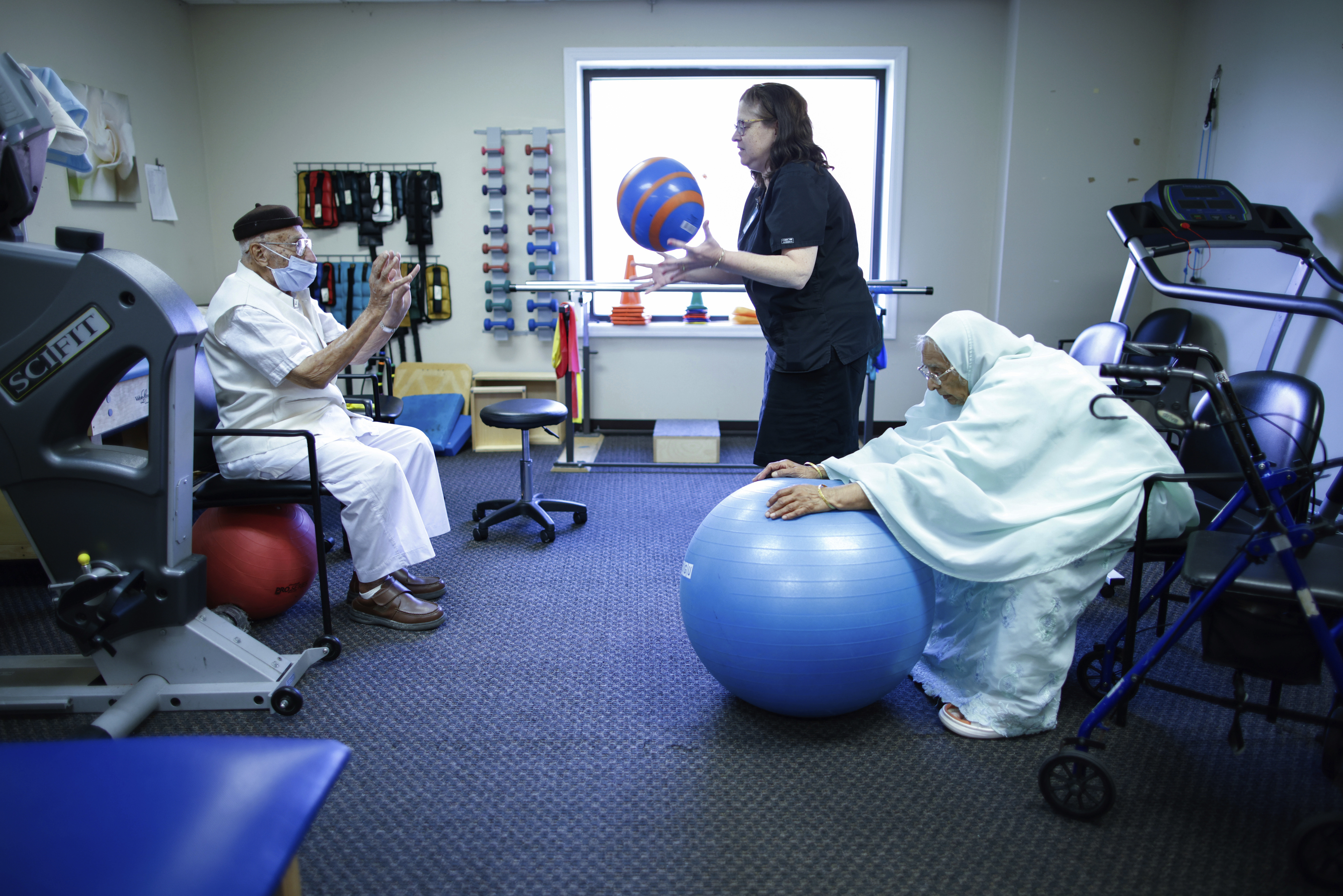 Mohamed, 84 (left) receives physical therapy with therapist Susan Fenyes (center) while his wife, Bibi, 84, stretches with a ball at Sunshine Adult Day Center in Bergenfield, N.J., Monday, Aug. 26, 2024.<br />(Kena Betancur / AP Photo)