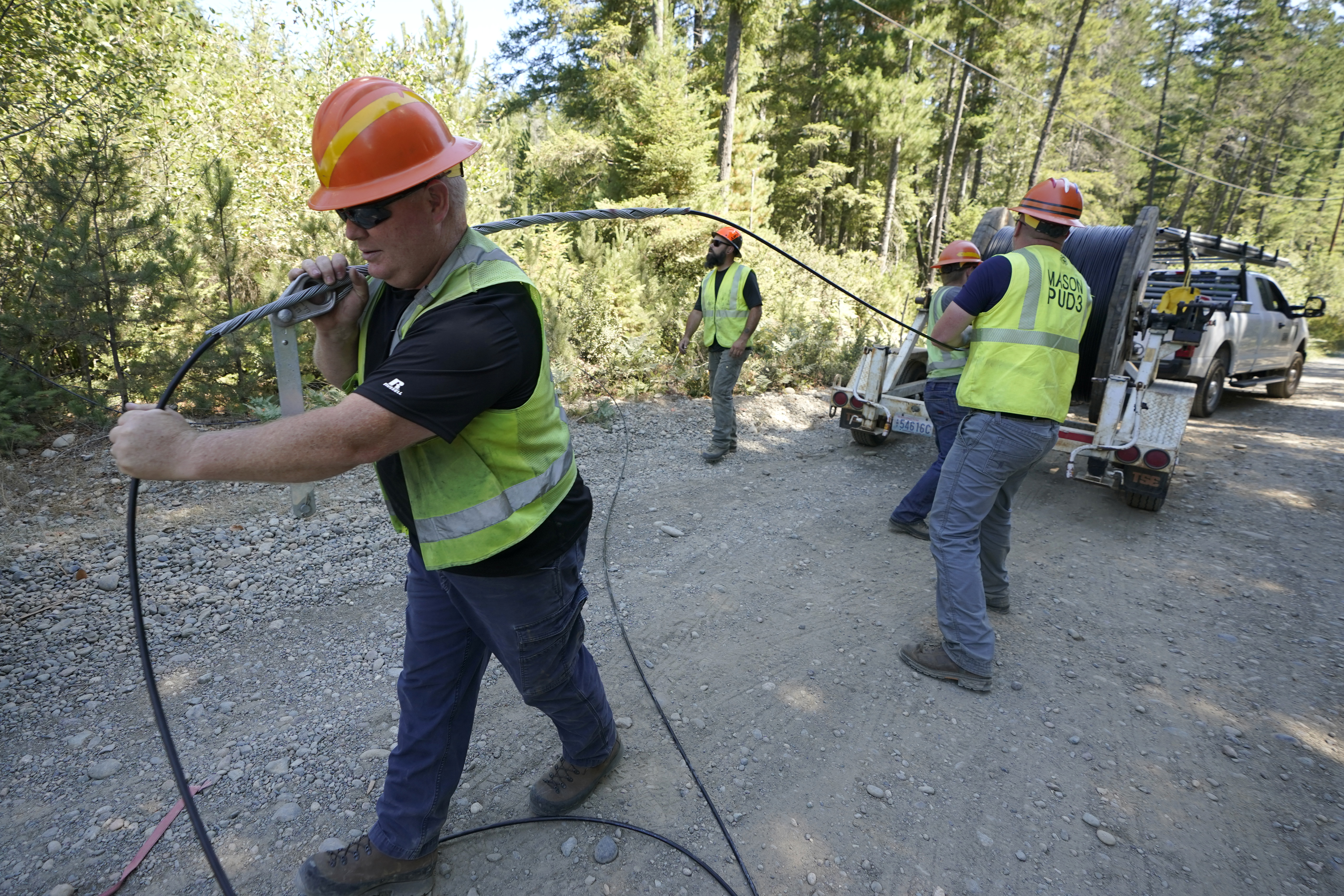 Carl Roath, (left) a worker with the Mason County (Wash.) Public Utility District, pulls fiber optic cable on a project to install broadband internet service in the area surrounding Lake Christine near Belfair, Wash., on Aug. 4, 2021. The Trump administration’s changes to a federal grant program meant to expand broadband access have disqualified hundreds of thousands of locations — including homes, businesses and community buildings — from receiving internet access.<br />(Ted S. Warren / AP Photo)