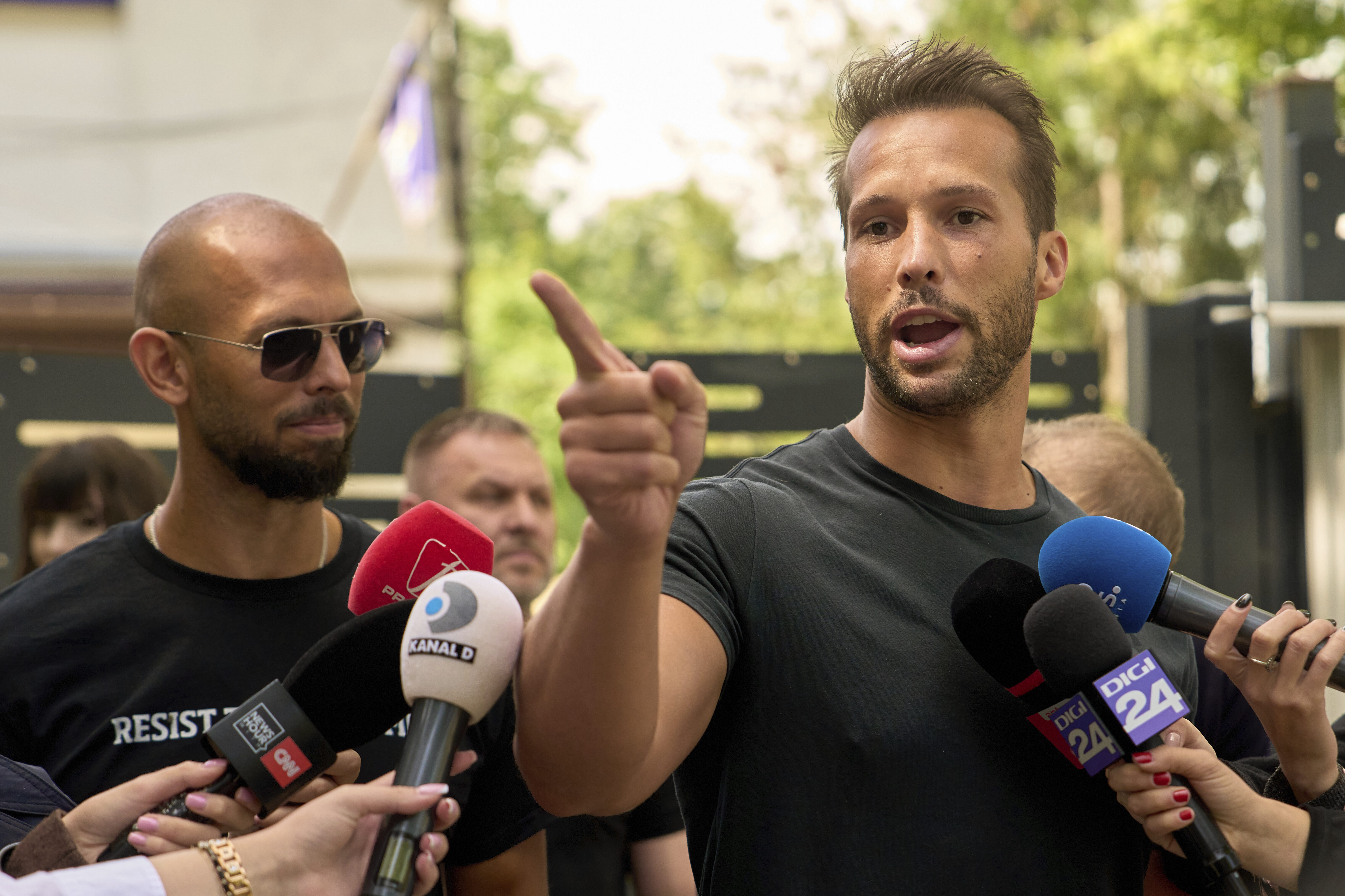 Andrew Tate (left) watches his brother Tristan speak, outside a police station in Voluntari, Romania, Wednesday, May 21, 2025.<br /> (Vadim Ghirda / AP Photo)