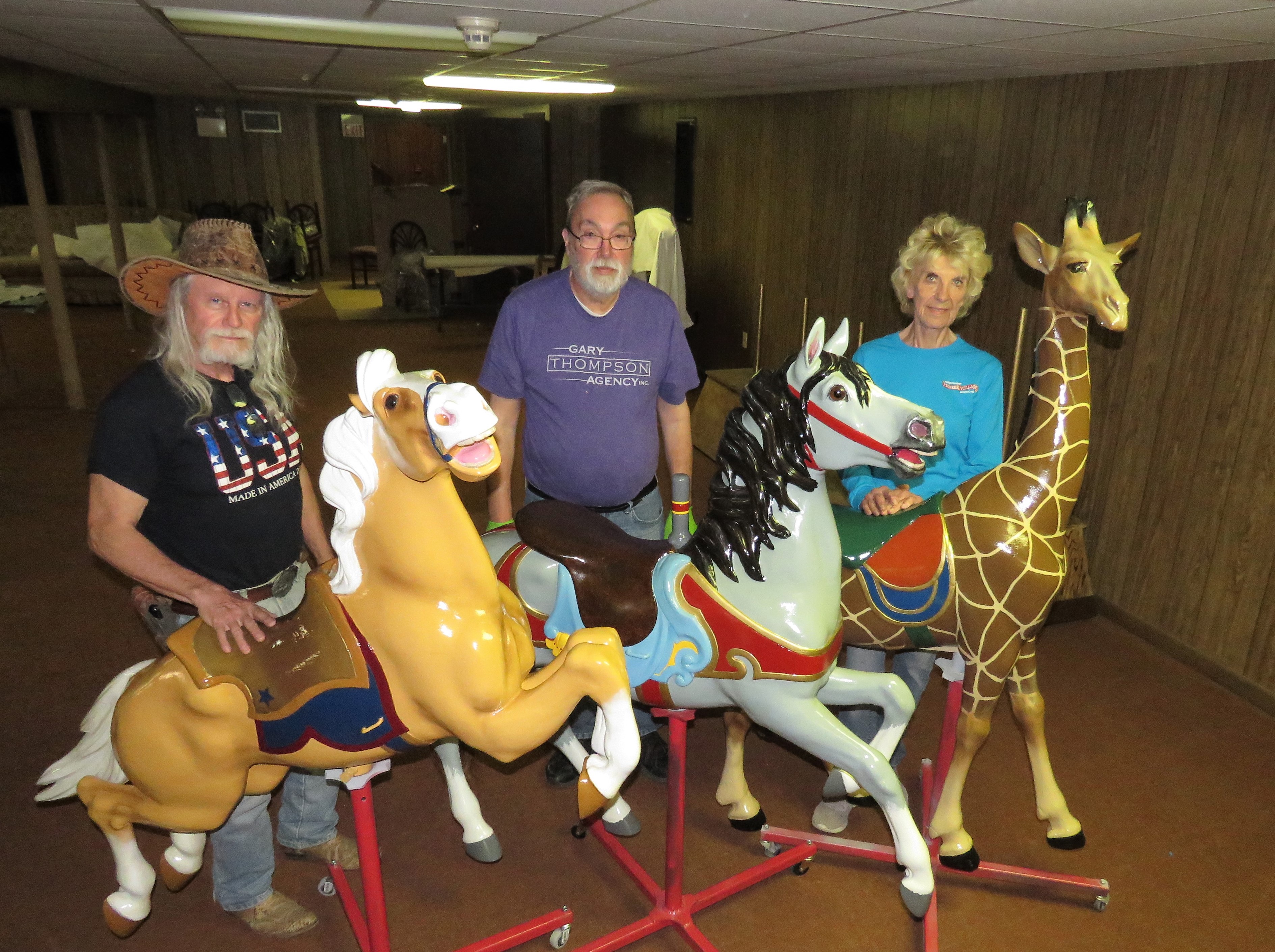 From left: Volunteers Brad Roberts of Heartwell, Sam Ridge of Minden and Jo Ann Weisman of Holdrege, stand by carousel figures restored by late May 2024. Other volunteers (not pictured) included Dave Borman of Kearney, Guy Johnson of Riverdale and Linda Kohl of Hastings. Their workspace is the old Pioneer Village Motel basement.<br />(Lori Potter / Flatwater Free Press)