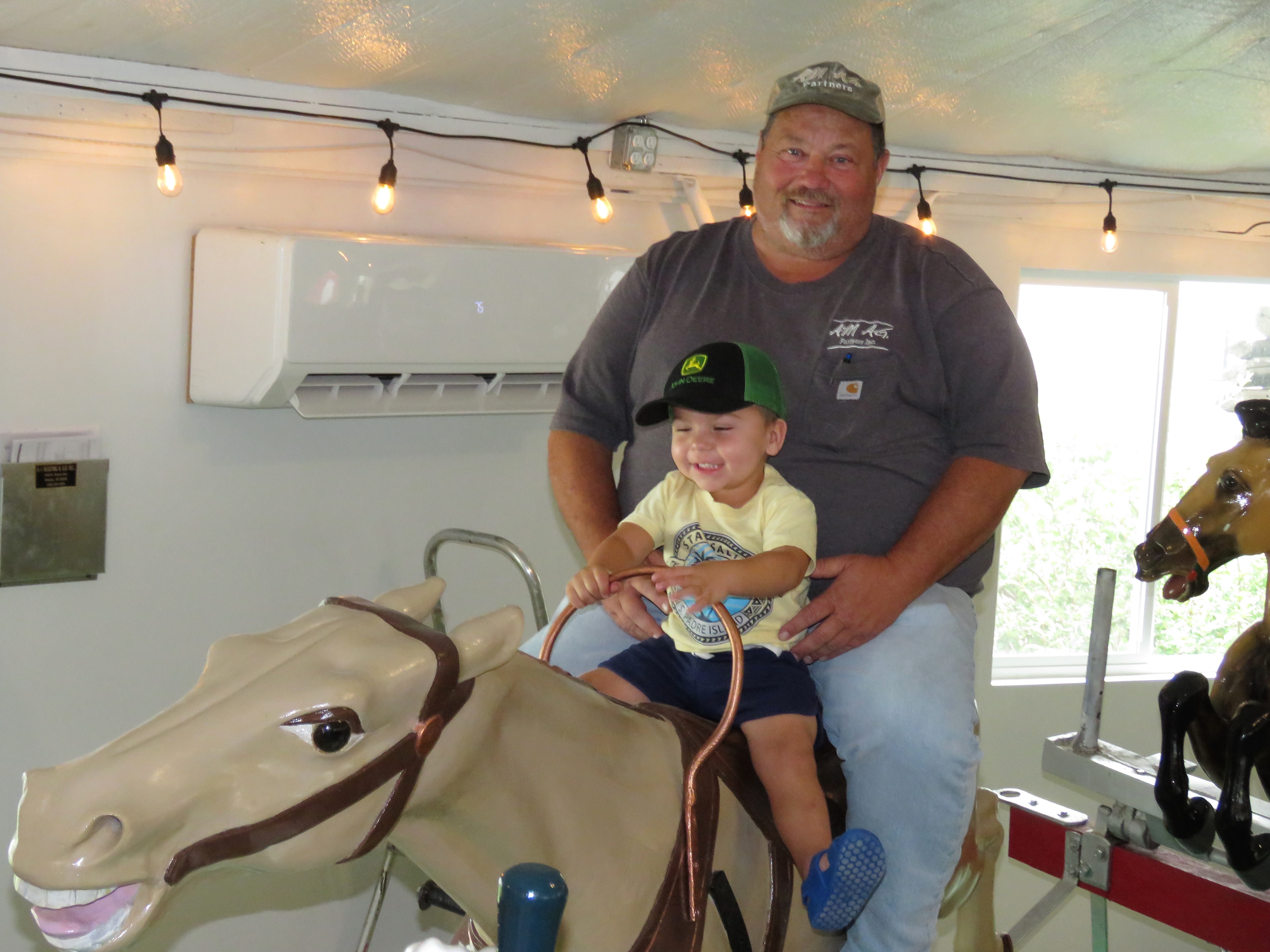 Waylon Petersen, 2, enjoyed riding a carousel horse Aug. 1 with his grandpa Jim Runions Jr. of Minden. Older generations of the family remember riding the old steam-powered carousel as kids.<br />(Lori Potter / Flatwater Free Press)