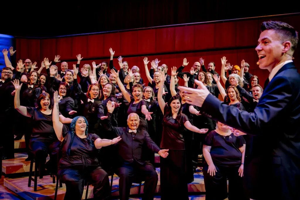 Members of the River City Mixed Chorus in the background and artistic director Barron Breland in the foreground gesture to the audience during the “Love out Loud” concert in June 2019.<br />(Photo courtesy of the River City Mixed Chorus)