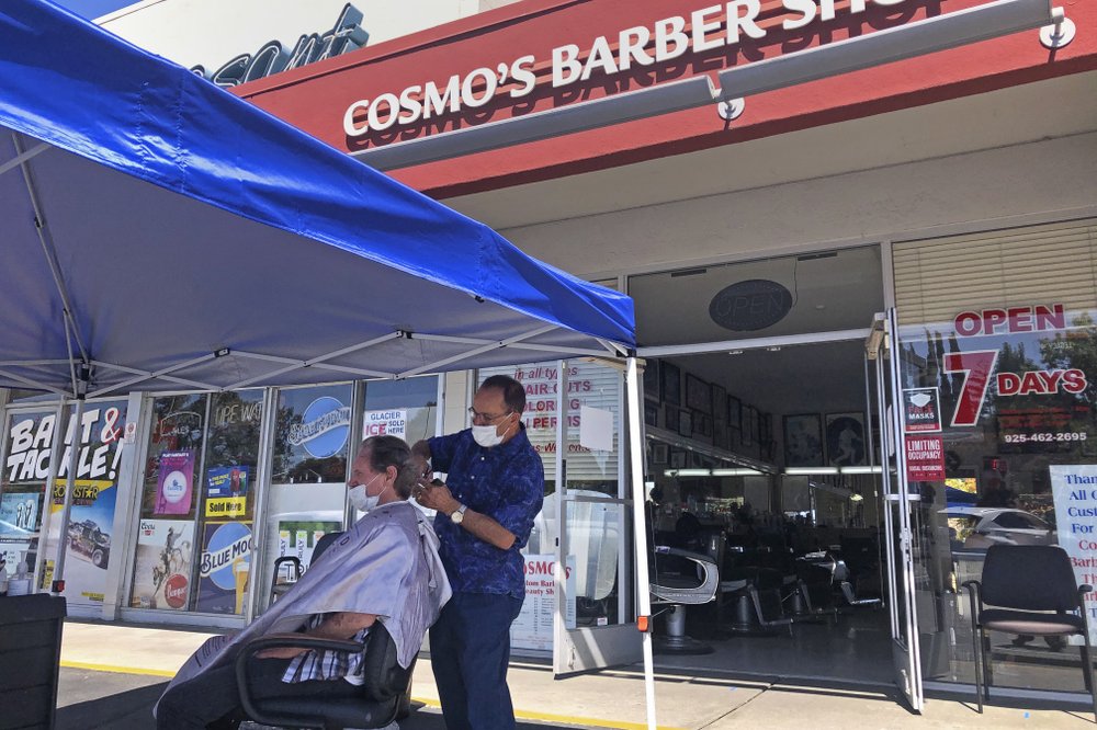 A customer of Cosmo’s Barber Shop receives a haircut in the parking lot in front of the shop in Pleasanton, Calif., July 22, 2020. Efforts to mitigate the coronavirus had a severe toll on many small businesses. Restaurants, hair salons, event planners and other businesses that rely on people being in close proximity were hard-hit, as were those tied to tourism. (AP)