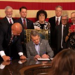 Nebraska Gov. Jim Pillen signs State Sen. Tom Brewer’s proposal to allow concealed carry of handguns without a permit or training on Tuesday, April 25, 2023. Brewer (at left) and nearly half of Nebraska’s state senators joined the signing. 
(Zach Wendling / Nebraska Examiner)