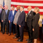 The justices of the Nebraska Supreme Court join Nebraska Gov. Jim Pillen (center left in a blue suit) and Lt. Gov. Joe Kelly (far left) for the elevation of Douglas County District Judge Derek Vaughn (center) to the Supreme Court. Vaughn’s colleagues, from left: are Justice John Freudenberg, Jason Bergevin, Jeffrey Funke (chief), William Cassel, Stephanie Stacy and Jonathan Papik, Nov. 10, 2025. 
(Zach Wendling / Nebraska Examiner)