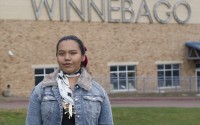 Tyler Free-LaMere, an enrolled member of the Winnebago Tribe of Nebraska, stands in front of the Winnebago Public Schools building in Winnebago on June 13. Free-LaMere recently was awarded a National Endowment for the Arts composer award for a composition created for her mother's Ho-Chunk dual-language immersion classroom and inspired by an Algonquin creation story about music. 
(Jerry L Mennenga / Flatwater Free Press)
