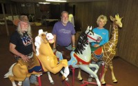 From left: Volunteers Brad Roberts of Heartwell, Sam Ridge of Minden and Jo Ann Weisman of Holdrege, stand by carousel figures restored by late May 2024. Other volunteers (not pictured) included Dave Borman of Kearney, Guy Johnson of Riverdale and Linda Kohl of Hastings. Their workspace is the old Pioneer Village Motel basement. 
(Lori Potter / Flatwater Free Press)