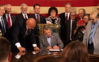 Nebraska Gov. Jim Pillen signs State Sen. Tom Brewer’s proposal to allow concealed carry of handguns without a permit or training on Tuesday, April 25, 2023. Brewer (at left) and nearly half of Nebraska’s state senators joined the signing. 
(Zach Wendling / Nebraska Examiner)