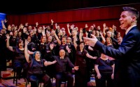 Members of the River City Mixed Chorus in the background and artistic director Barron Breland in the foreground gesture to the audience during the “Love out Loud” concert in June 2019. 
(Photo courtesy of the River City Mixed Chorus)