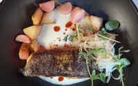Crispy-skinned striped sea bass is served over a coconut ginger sauce and roasted radishes and potatoes finished with bean sprouts and a Sichuan peppercorn oil. 
(Sarah Baker Hansen / Flatwater Free Press)