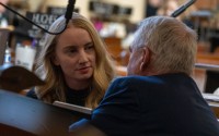 State Sen. Megan Hunt of Omaha listens to State Sen. Dave Murman of Glenvil kneeling at her desk on March 12, 2024. 
(Zach Wendling / Nebraska Examiner)